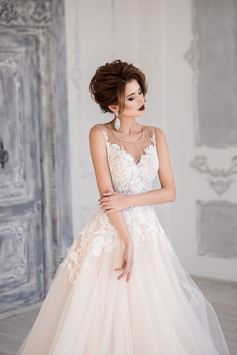 Morning of the bride. A beautiful bride stands in a wedding dress. Wedding hairstyle and makeup. Dress with lace.