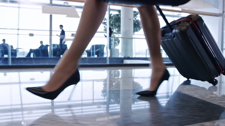 Legs of woman wearing high heels walking in airport with her wheeled luggage