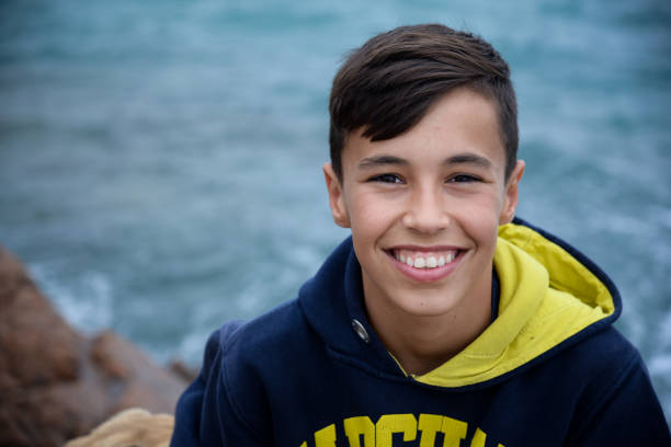 Smiled teenage boy hugs his dog and looking at camera on rocks near the sea.