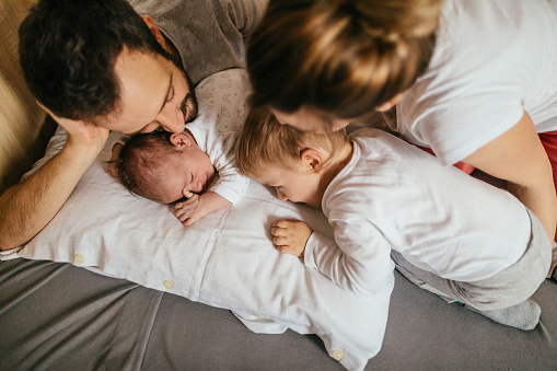 Photo of a young family getting to know their new family member - little newborn baby, and enjoy their moments together while still in pajamas in their bedroom
