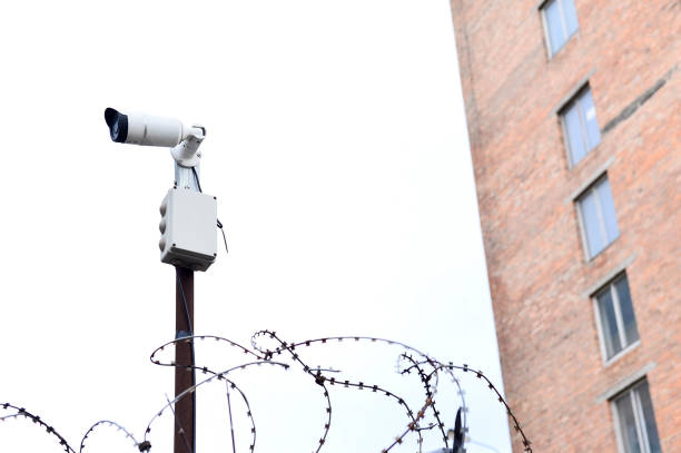 istock Camera video surveillance on the building background mounted on a brick wall, fenced with barbed wire. 930505198