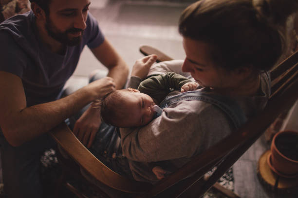 Spending time with our new family member Photo of a young mother holding her newborn baby, while sitting in a rocking chair. Father is sitting next to them on the floor. rocking chair stock pictures, royalty-free photos & images