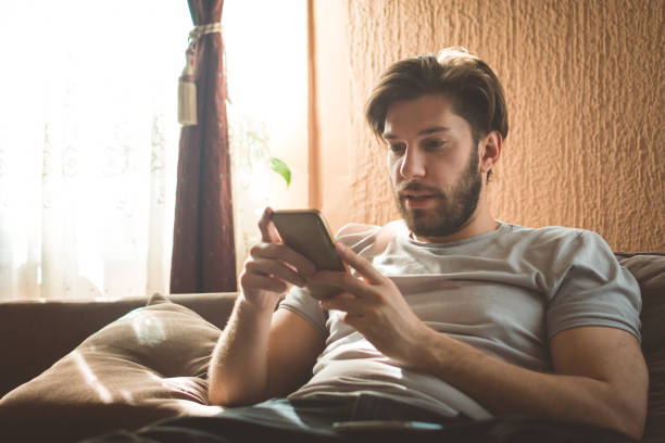 istock Young man sitting on sofa in living room and using phone 930508778