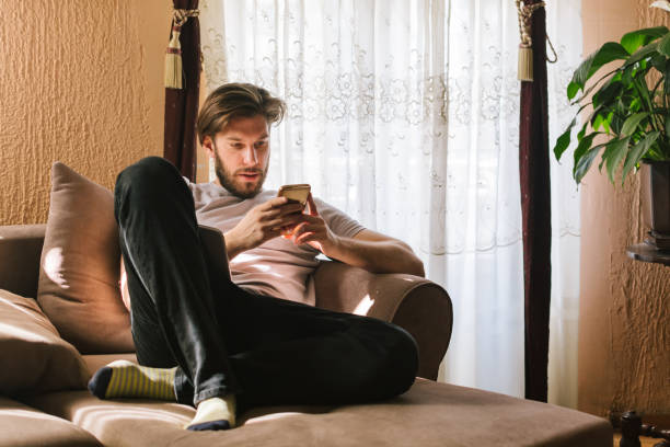 istock Young man sitting on sofa in living room and using phone 930508812