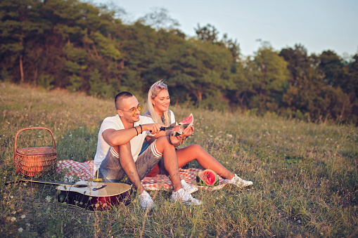Happy young couple sitting on picnic blanket in nature and eating watermelon