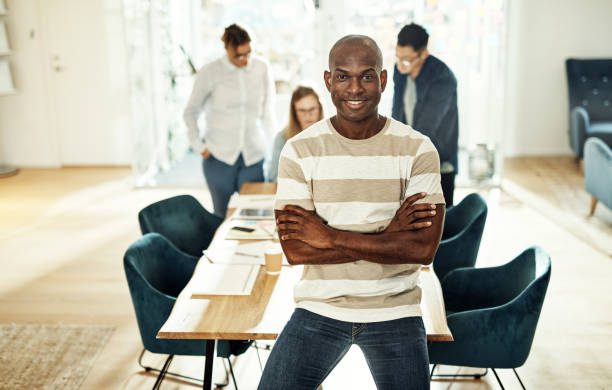 istock Young designer leaning on a table with coworkers behind him 930515044