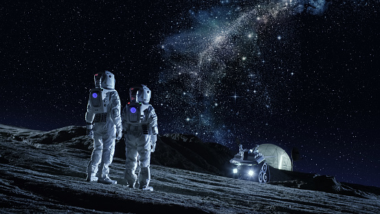 Soporte de dos astronautas en trajes espaciales en el planeta y mirando la la Galaxia Vía Láctea. En la Base Lunar de fondo con cúpula geodésica. Colonización de la luna y concepto del espacio recorrido. photo