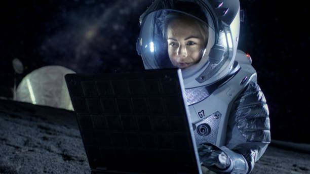 istock Female Astronaut Wearing Space Suit Works on a Laptop, Exploring Newly Discovered Planet, Communicating with the Earth. In the Background Space Habitat. Colonization Concept. 930523182