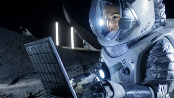 istock Female Astronaut Wearing Space Suit Works on a Laptop, Exploring Newly Discovered Planet, Communicating with the Earth. In the Background Her Space Habitat. Colonization Concept. 930523184
