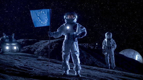 Mujer astronauta plantando la bandera de la Unión Europea en el planeta alienígena. En el fondo su miembro de la tripulación, la estación de vida y exploración Rover. Recorrido de espacio y concepto de colonización del Sistema Solar. photo