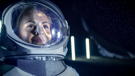 Portrait of the Beautiful Female Astronaut on the Alien Planet. Earth Reflection on her Helmet. In the Background Living Habitat. Space Travel, Extraterrestrial Exploration and Solar System Colonization Concept.