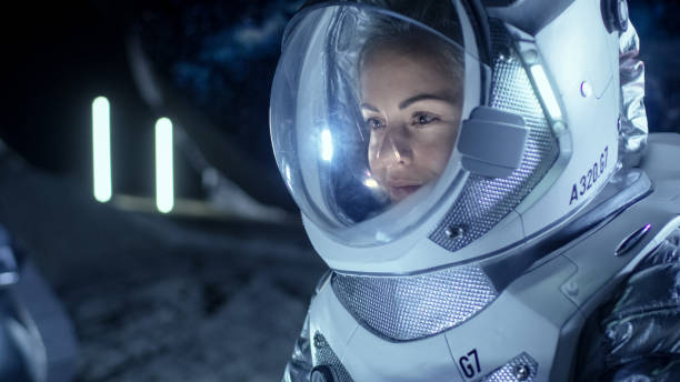 istock Female Astronaut Wearing Space Suit Works on a Laptop, Exploring Newly Discovered Planet, Communicating with the Earth. In the Background Her Crew Member and Living Habitat. Extraterrestrial Colonization Concept. 930523284