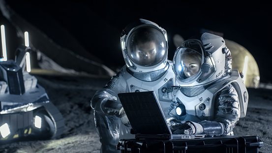 Two Astronauts Wearing Space Suits Work on a Laptop, Exploring Newly Discovered Planet, Send Communicating Signal to Earth. Space Travel, Interstellar Exploration and Colonization Concept.