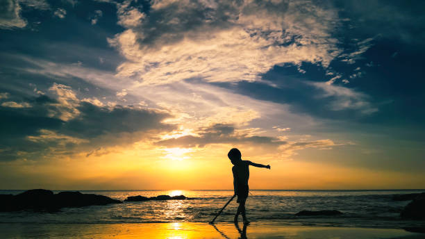 Young boy dragging stick at sunrise - fotografia de stock