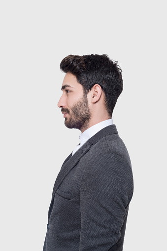Profile view of young businessman in suit looking away over gray background. Vertical composition. Studio shot.