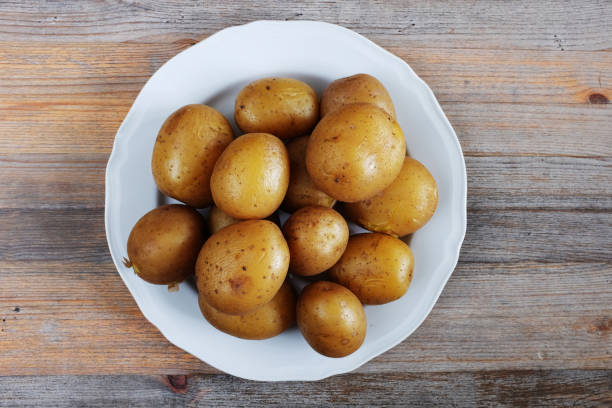 patate bollite nelle loro pelli su un piatto, sfondo di legno - foto stock