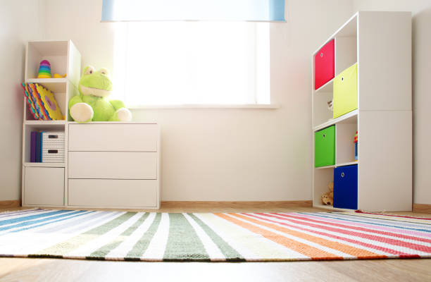 Colourful children rooom with white walls and furniture Colourful children rooom with white walls and furniture. Rainbow carpet at home interior with a window. playroom stock pictures, royalty-free photos & images