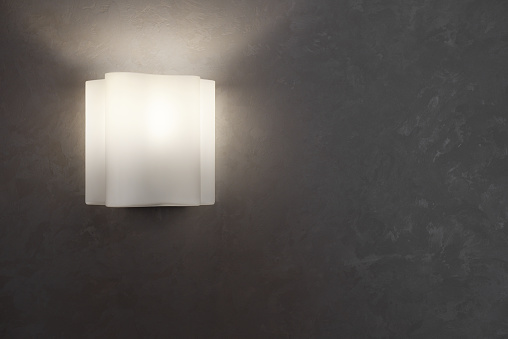 A beautiful wavy sconce is mounted on the wall with a texture. Lit in the evening.