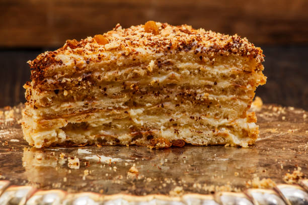 istock Napoleon's cake with custard is decorated with raisins and grated chocolate on a silver platter on a wooden table. Dessert Napoleon cake chopped. Napoleon cake tasty close-up. 930565146
