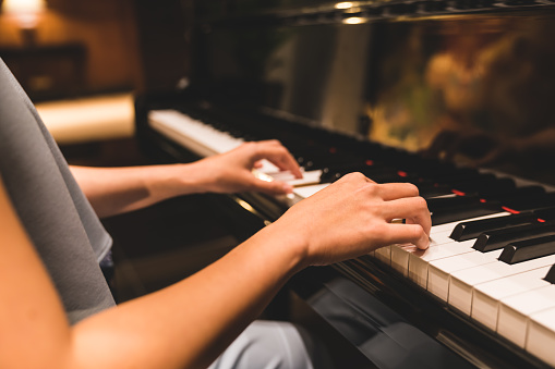 Asian woman hand playing keyboard of a piano in romantic atmosphere. Music instrument, solo pianist, song composer, hobby, practice study, or wedding event concept
