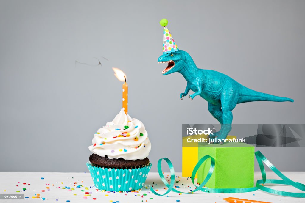 Dinosaur Birthday Party Toy Dinosaur blowing out a Birthday candle with cup cake on a gray background Birthday Stock Photo