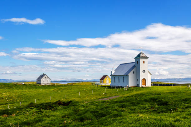 flateyjarkirkja kościół i kilka domów mieszkalnych z łąką na pierwszym planie i fiord morski z błękitnym niebem w tle, flatey, islandia - flatey zdjęcia i obrazy z banku zdjęć