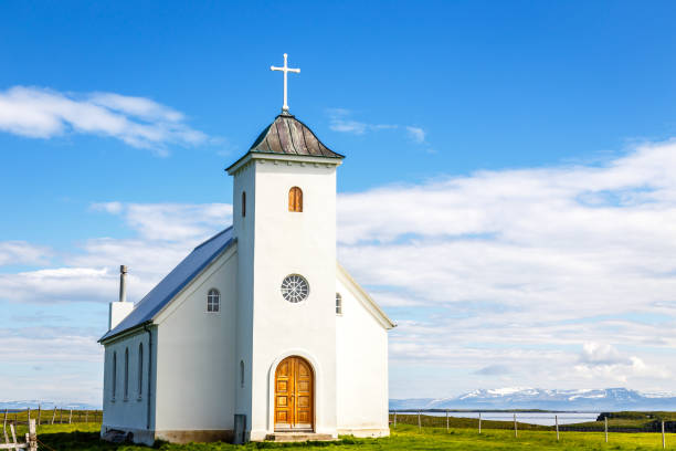 flateyjarkirkja biały kościół luterański z łąką na pierwszym planie i fiordem morskim z błękitnym niebem i górami w tle, flatey, islandia - flatey zdjęcia i obrazy z banku zdjęć