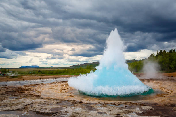 famosa fontana strokkur geyser eruzione di acqua blu calda con cielo nuvoloso e paesaggio islandese circostante, islanda - fumarole foto e immagini stock