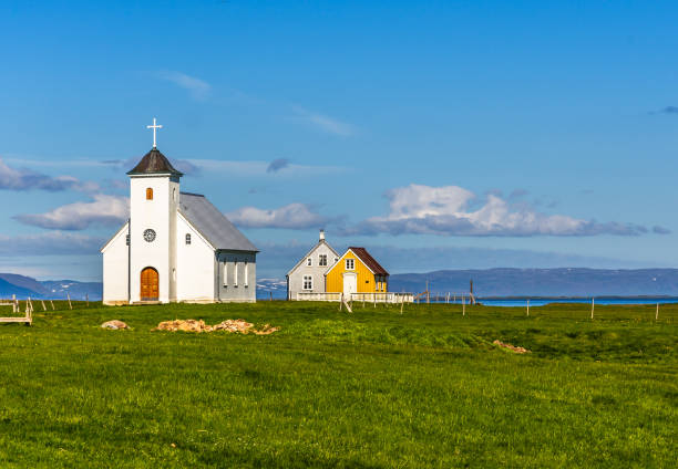 flateyjarkirkja biały kościół luterański i kilka żywych chat z łąką na pierwszym planie i fiord morski z błękitnym niebem w tle, flatey, islandia - flatey zdjęcia i obrazy z banku zdjęć