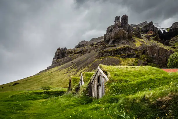 Photo of Icelandic turf houses covered with grass and cliffs in the background near Kalfafell vilage, South Iceland