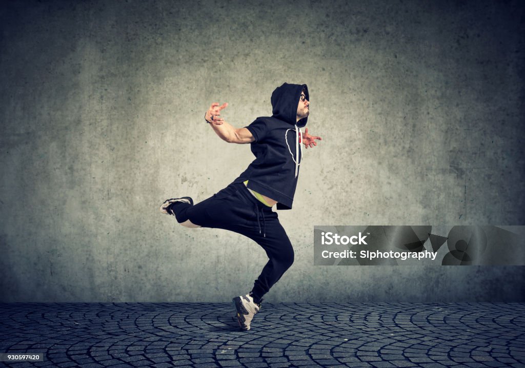 Young man break dancing on wall background Stylish young man in trendy sportive clothing performing street dance with on gray wall background. Dancing Stock Photo