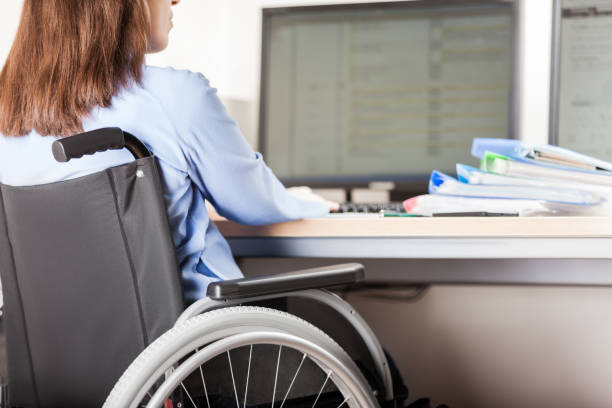 Disabled woman sitting wheelchair working office desk computer stock photo