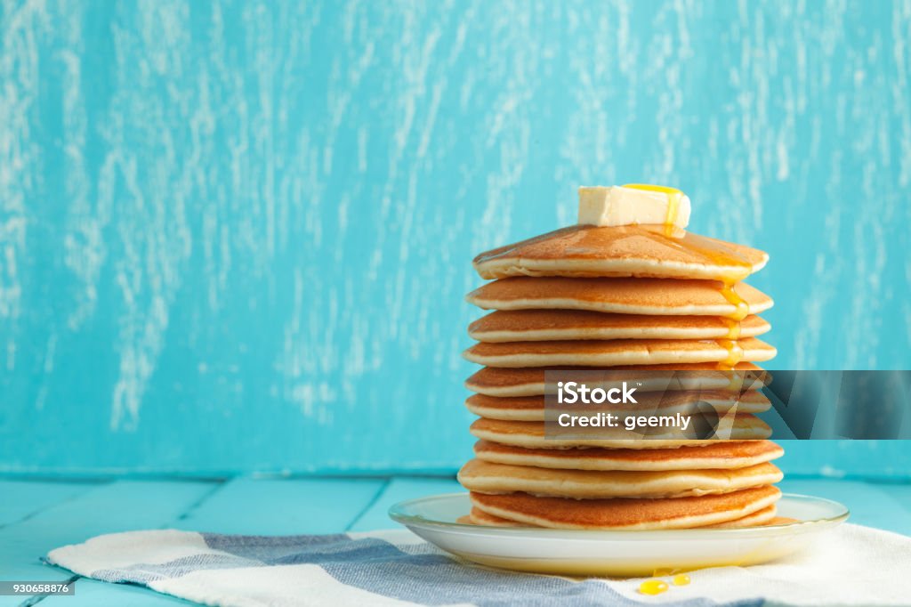 Stack of pancake with honey and butter on top Stack of pancakes with honey and piece of butter on plate which stands on napkin on blue wooden table. Copyspace. Concept of shrovetide treats. Selective focus Pancake Stock Photo