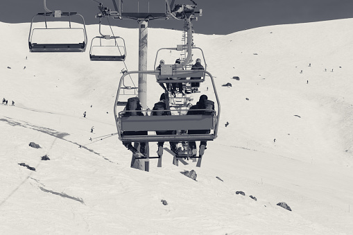 Skiers and snowboarders on chair-lift and snowy ski slope at cold winter day. Caucasus Mountains, Georgia, region Gudauri. Black and white toned image.