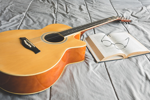 Orange acoustic guitar and open book with eyeglasses