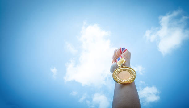 istock hand raised and holding gold medal against sky. award concept 930709092