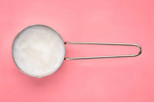 measuring metal scoop of coconut cooking oil on a pink background