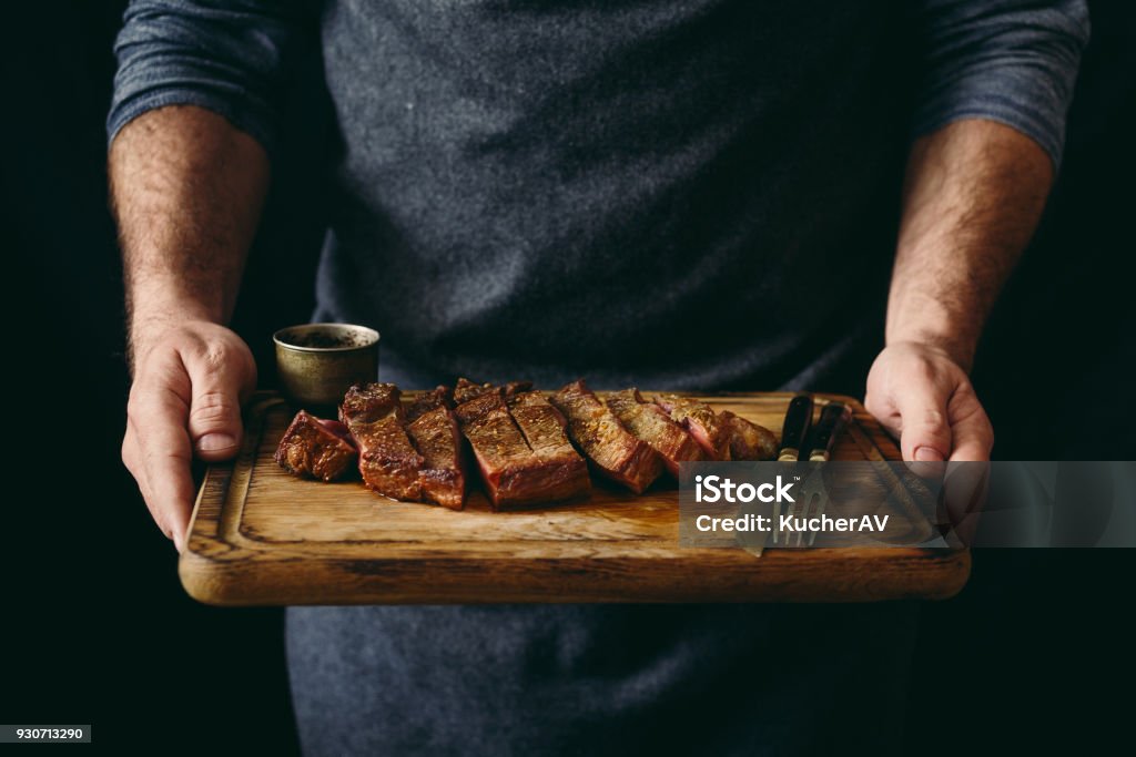 Man holding juicy grilled beef steak with spices on cutting board Meat Stock Photo