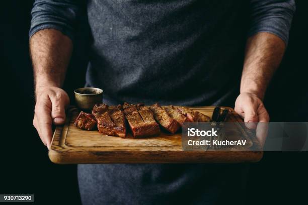 Man Holding Juicy Grilled Beef Steak With Spices On Cutting Board Stock Photo - Download Image Now