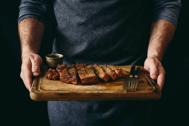 man holding juicy grilled beef steak with spices on cutting board - steak meat barbecue grilled imagens e fotografias de stock