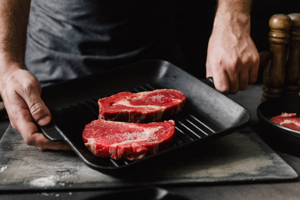 hombre cocinar bistecs masculinas manos sosteniendo una sartén parrilla con filetes de carne en cocina - barbecue grill fotos fotografías e imágenes de stock
