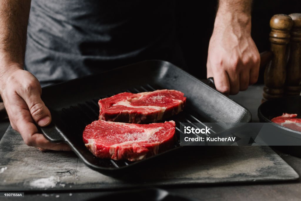 Homem machos mãos segurando uma panela de grelhar com bifes na cozinha a cozinhar bifes - Foto de stock de Carne royalty-free