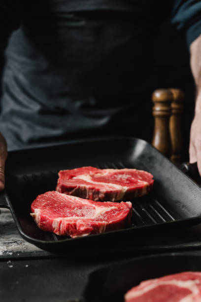 istock Male hands holding a grill pan with beef steaks on kitchen Man cooking beef steaks 930715566