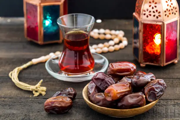 Ramadan Kareem Festive, close up of dates on wooden plate and prayer beads with oriental Lantern lamps and cup of black tea on wood background. Islamic Holy Month Greeting Card