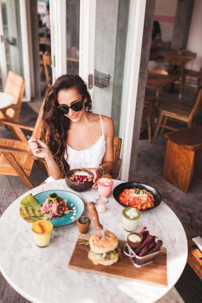 junge lächelnde frau mit frühstück im stilvollen straßencafé. smoothie-schüssel, matcha latte, tacos und burger - breakfast eating people teens stock-fotos und bilder