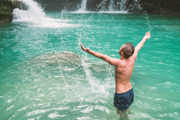 istock Young man splashing water in waterfall, Philippines 930728684