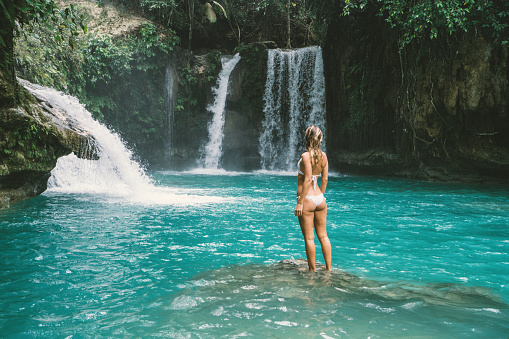 Young woman contemplating a beautiful waterfall on the Cebu Island in the Philippines. People travel nature loving concept. One person only enjoying outdoors and tranquillity in a peaceful environment