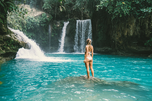 Young woman contemplating a beautiful waterfall on the Cebu Island in the Philippines. People travel nature loving concept. One person only enjoying outdoors and tranquillity in a peaceful environment