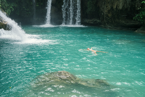 Young woman floating on a beautiful waterfall pool on the Cebu Island in the Philippines. People travel nature concept. One person only enjoying outdoors and tranquillity in a peaceful environment