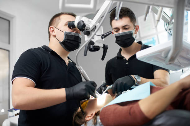 istock Male dentist in a black uniform fixing patient's teeth while another one is helping him with instruments 930758884